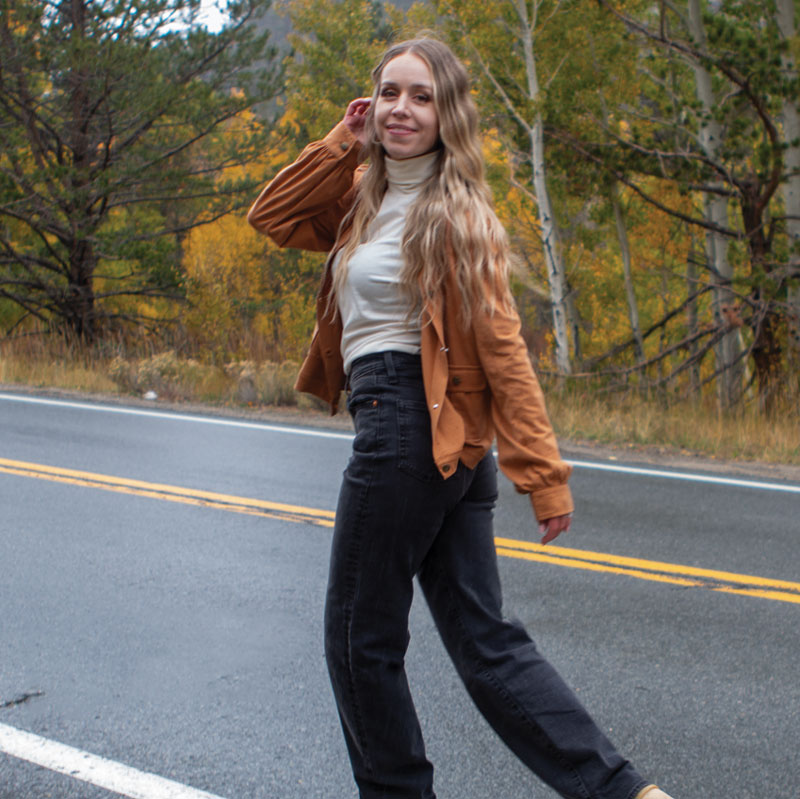 Woman walking along road through forest during fall.