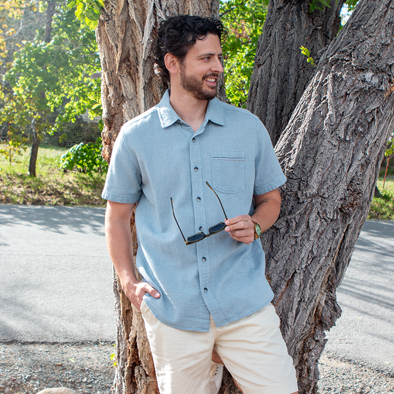 Man standing against tree with sunglasses in hand.