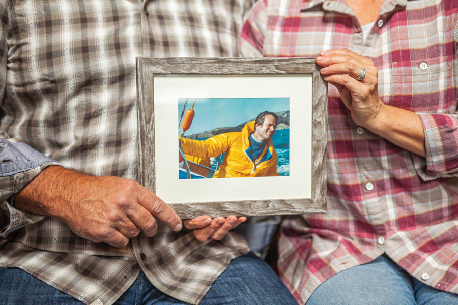 Kirsch siblings holding framed photo of father on sail boat.