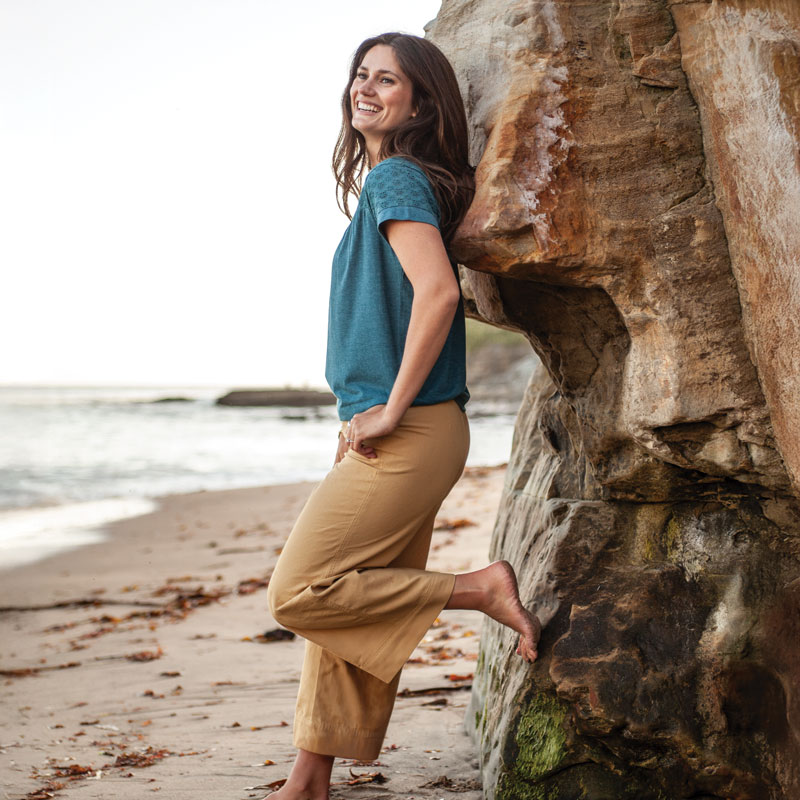 Woman leaning against rock on ocean shore.