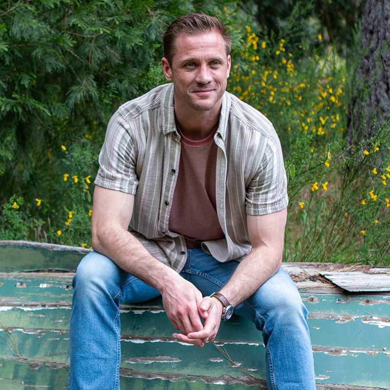 Man sitting on old rustic canoe outdoors.